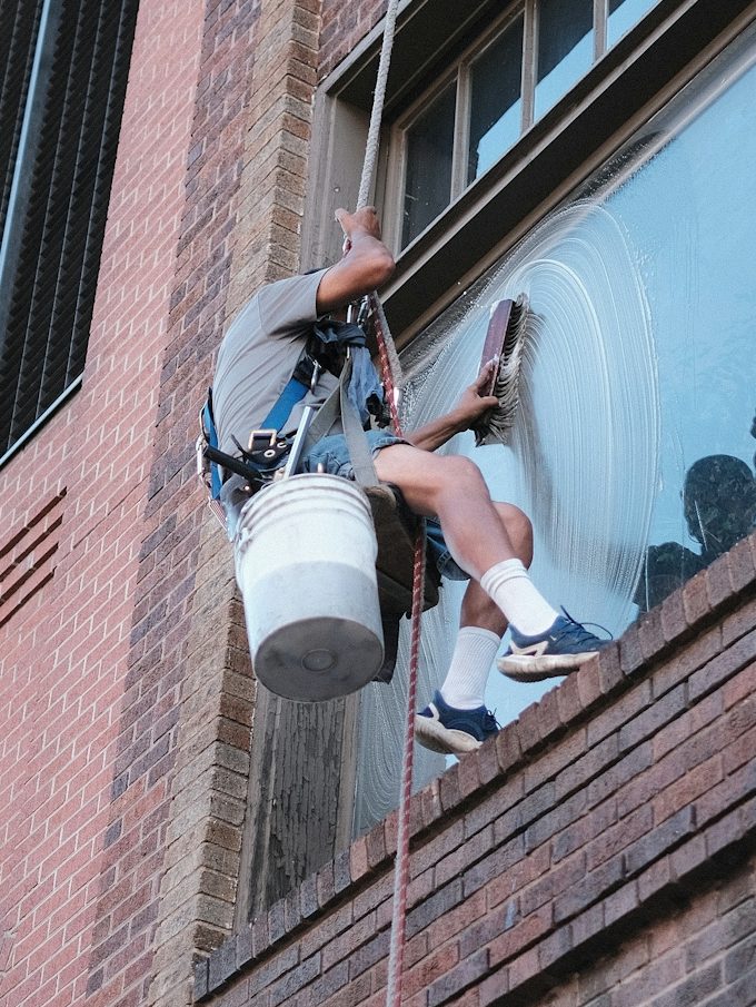 Ein Fensterputzer hängt an einem Seil und reinigt eine Fensterfläche.